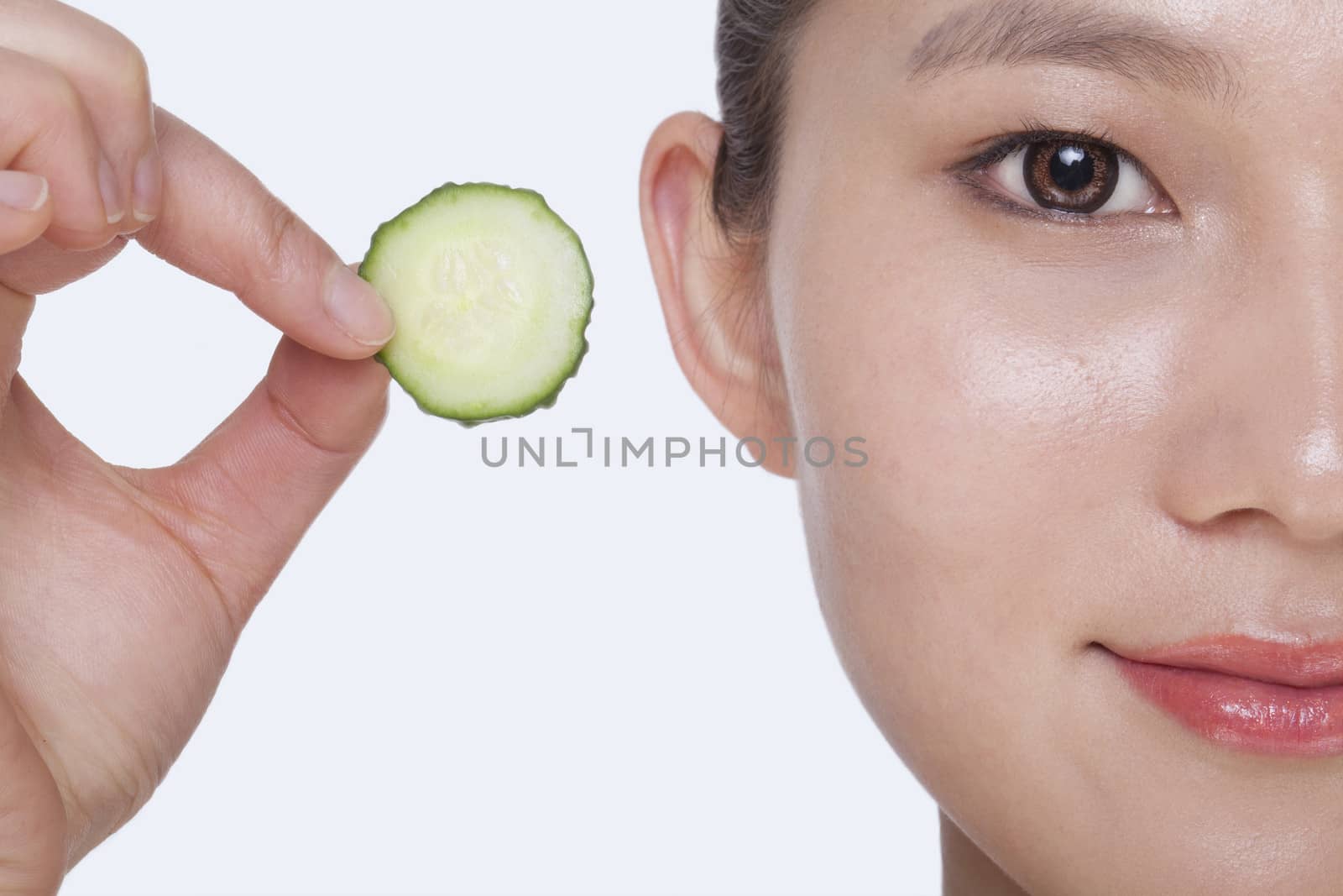 Close up of smiling young woman holding up a cucumber slice, studio shot by XiXinXing