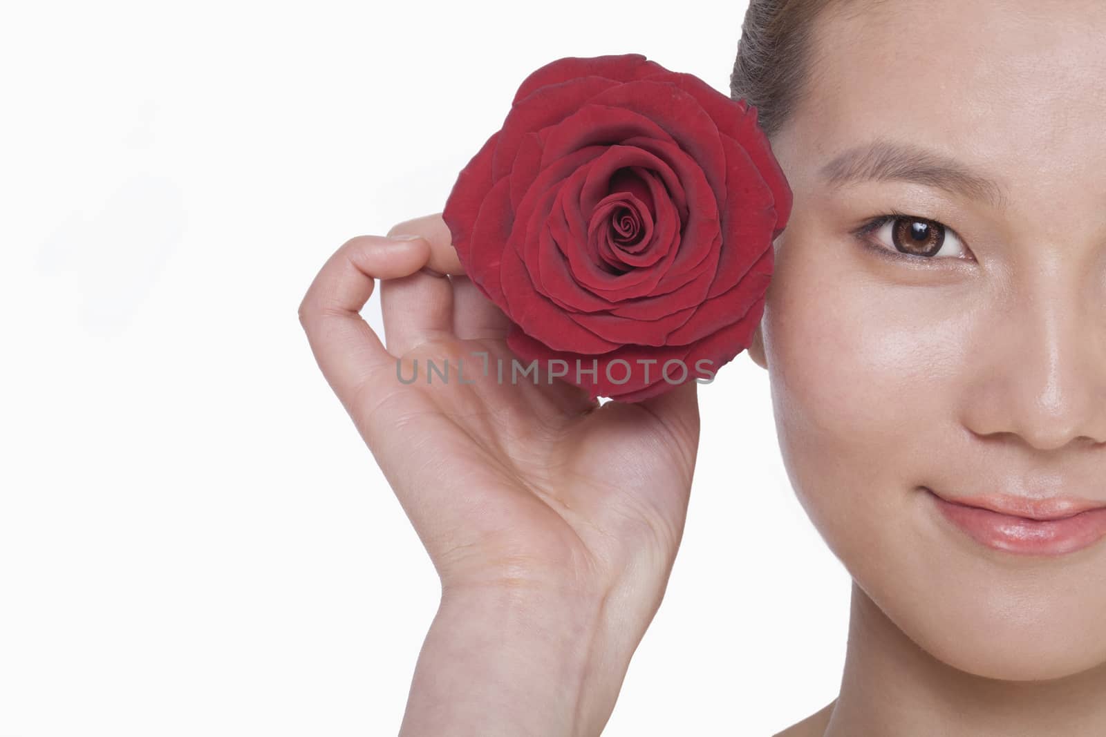 Smiling young woman holding up a red rose next to her ear, studio shot by XiXinXing