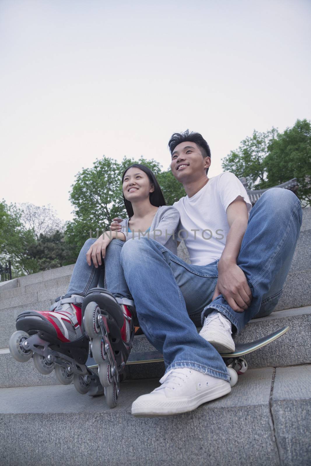 Young happy couple sitting and resting on concrete steps outside with a skateboard and roller blades