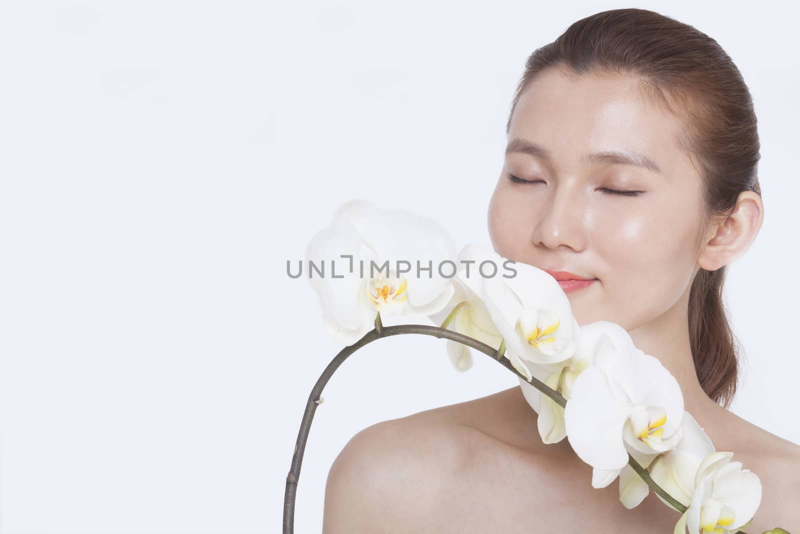 Shirtless young woman with eyes closed smelling a bunch of beautiful white flowers, studio shot by XiXinXing