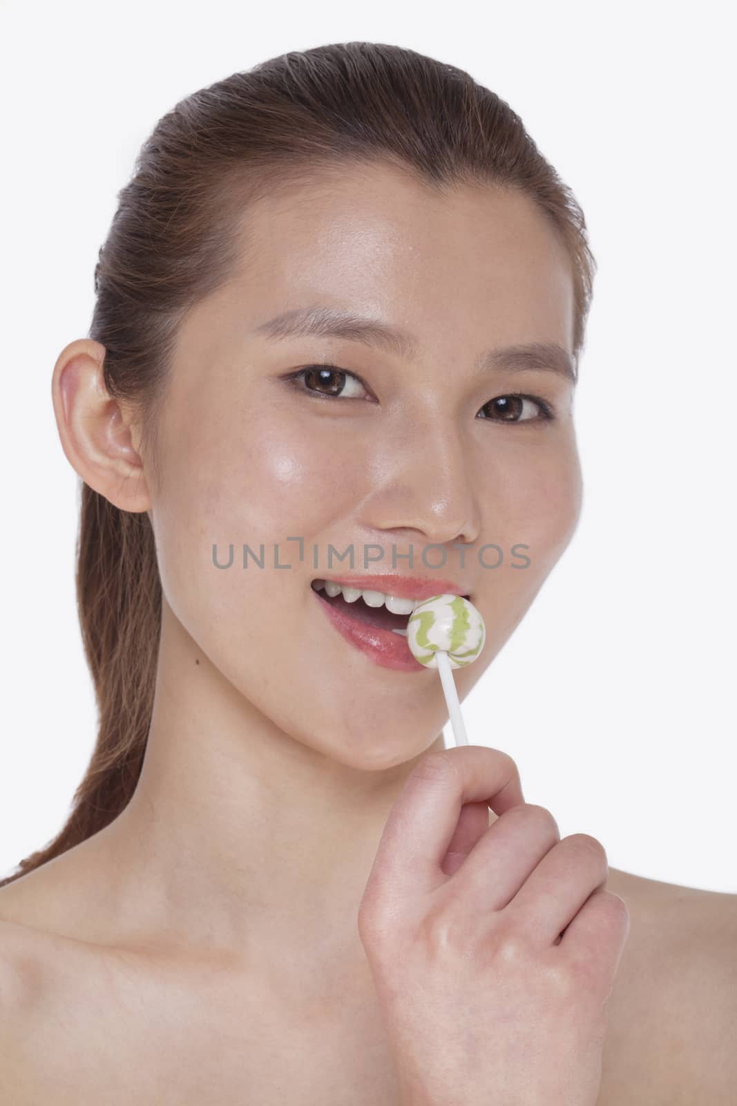 Smiling young woman looking into camera and licking a lollipop, studio shot