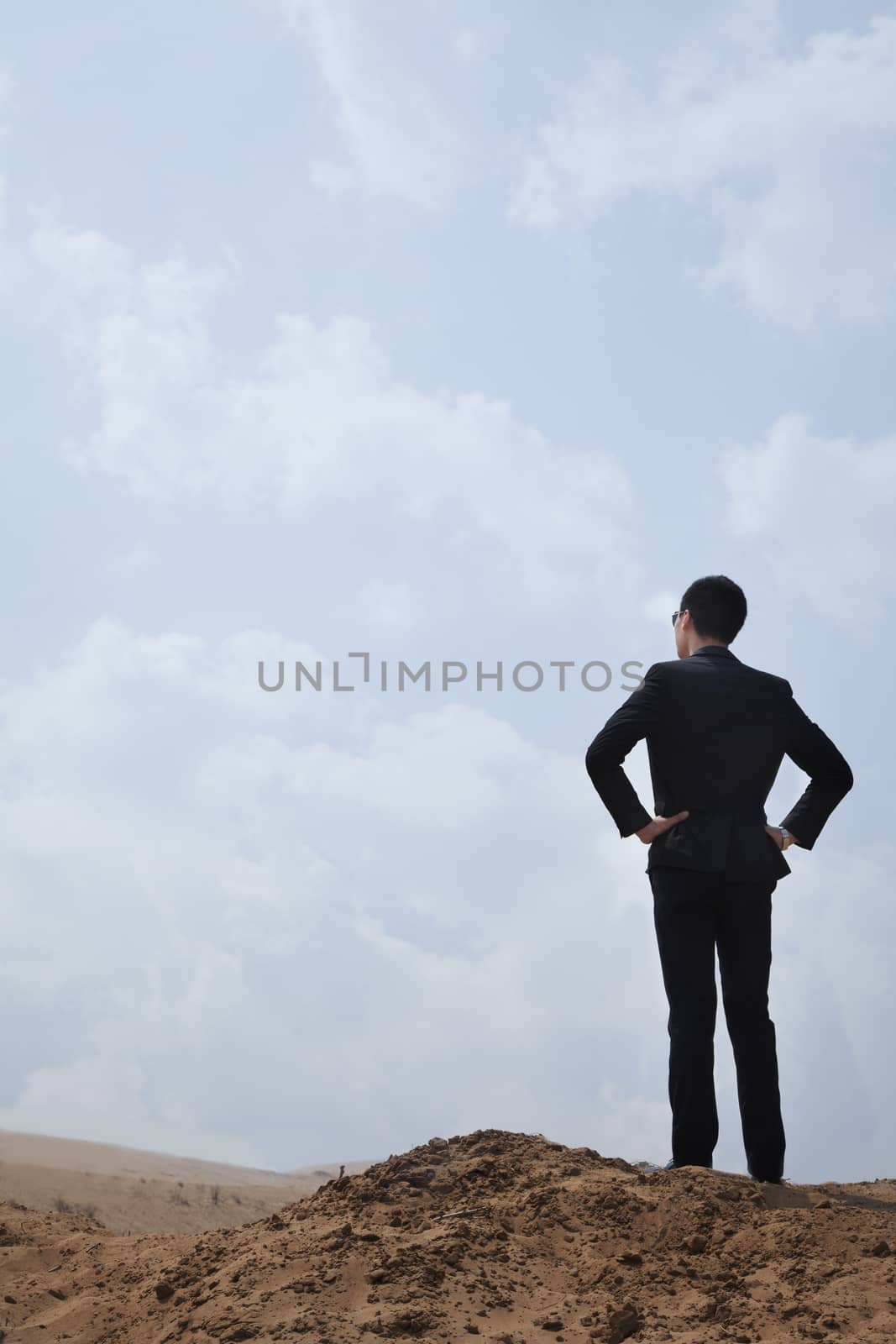 Young businessman standing with hands on hips looking out over the desert