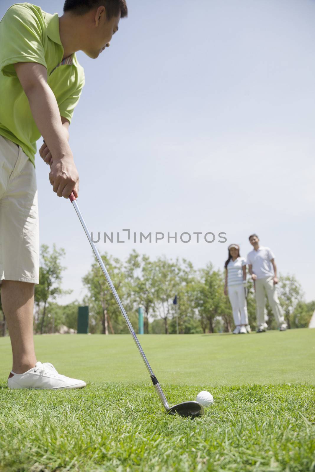 Young man hitting a ball on the golf course, man and woman in the background