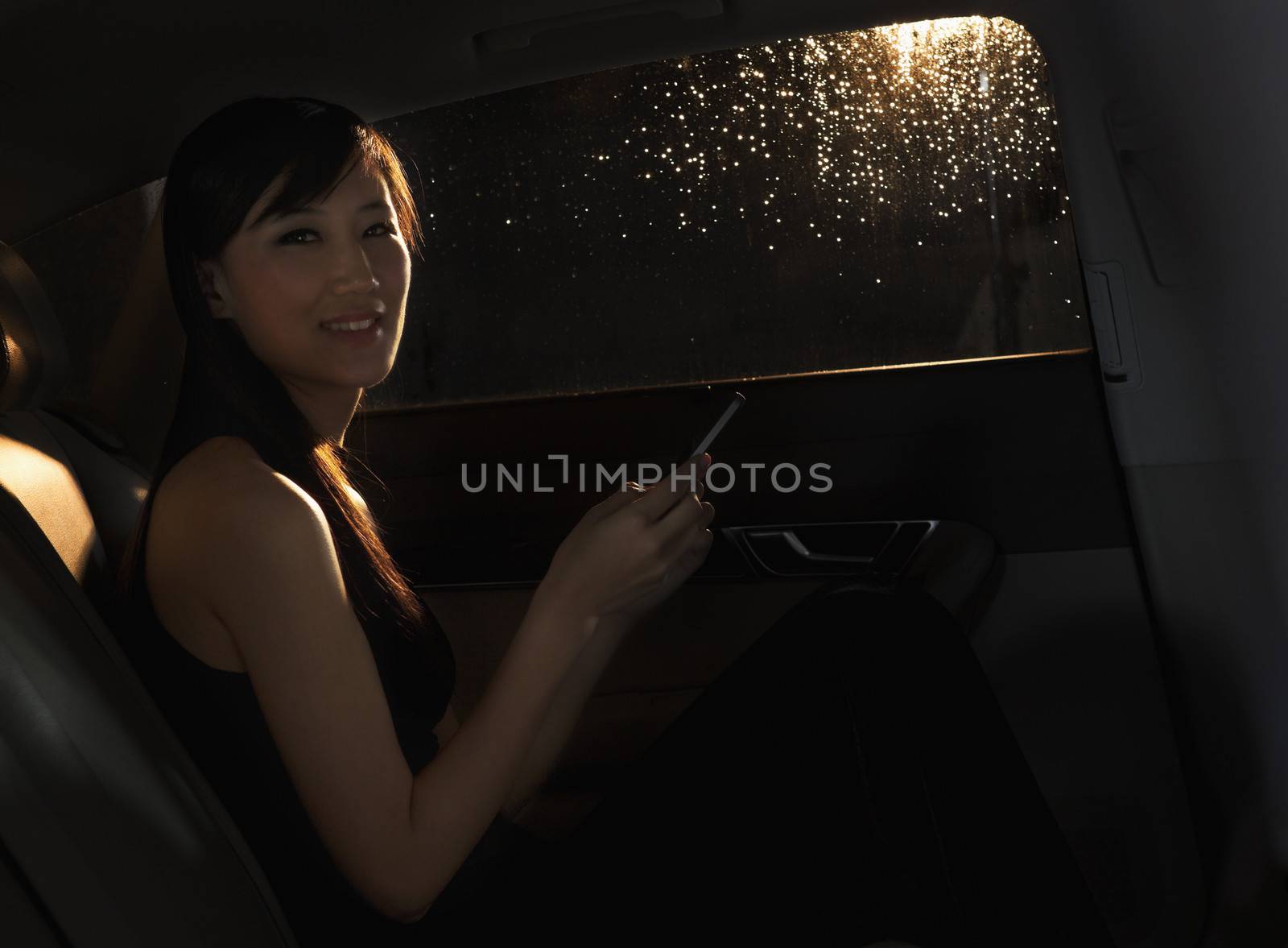 Young woman sitting in the car, on her phone, and looking at the camera on a rainy night in Beijing by XiXinXing