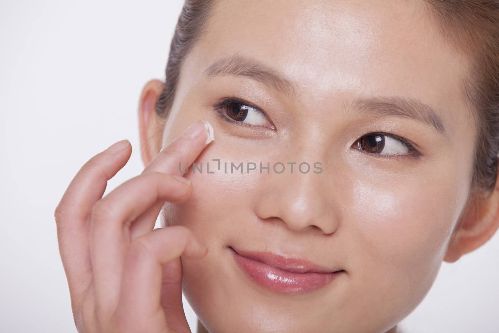 Close up on the face of a smiling young woman applying cream to her face, studio shot