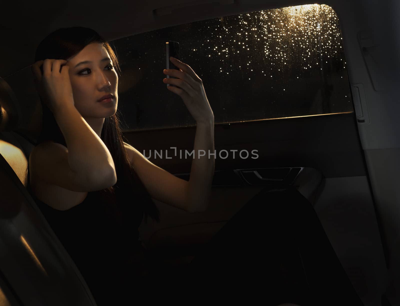 Young woman sitting in her car and checking her hair in the phone before going out on a rainy night in Beijing