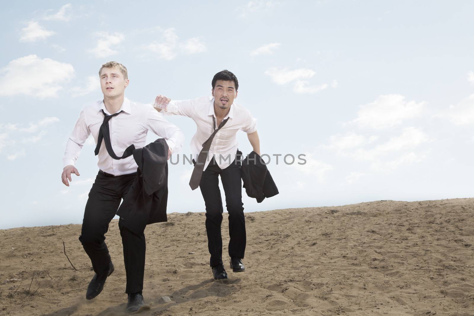 Two young businessmen running and exhausted in the desert, holding jackets by XiXinXing