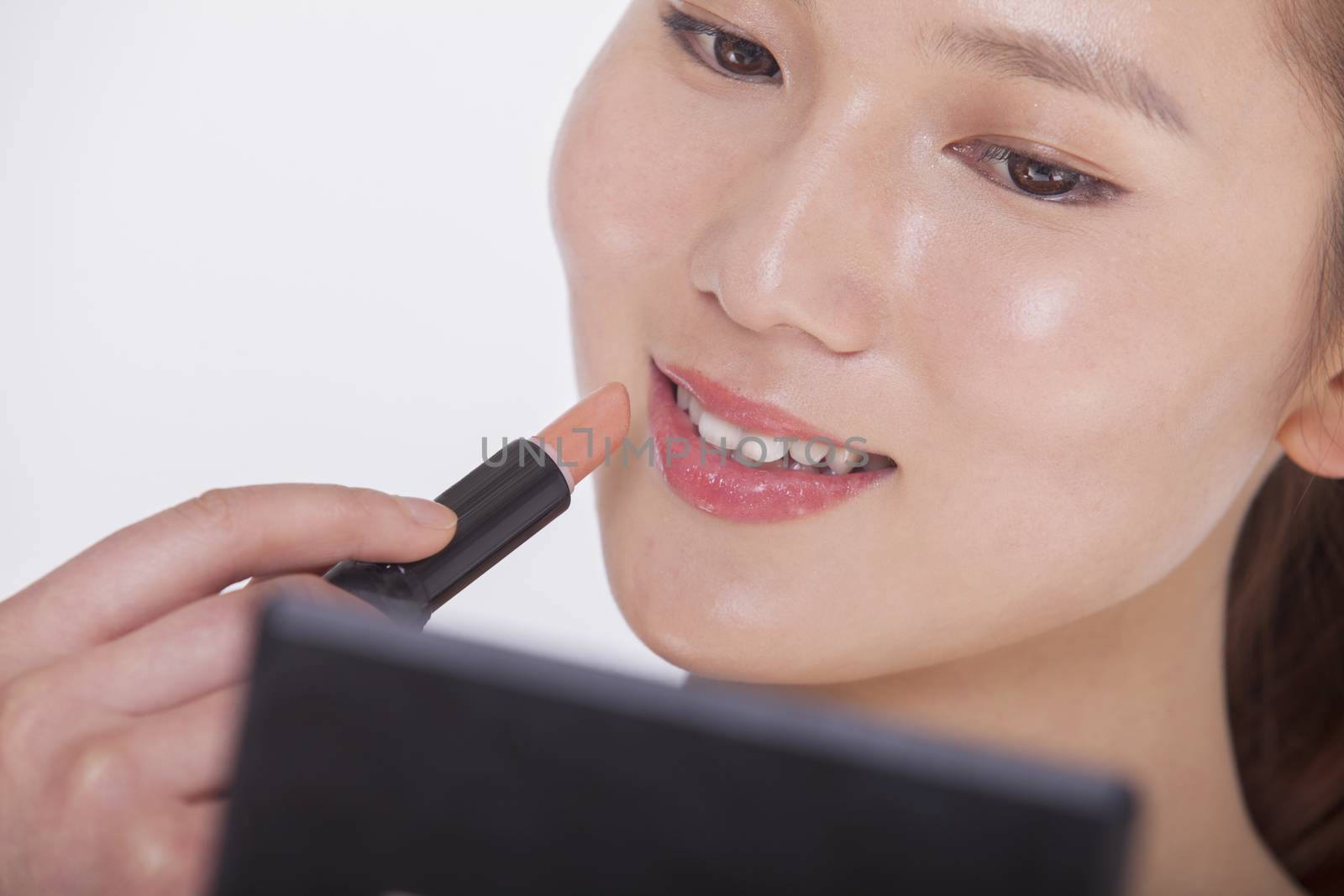 Close up of young woman applying lipstick in a mirror, studio shot by XiXinXing