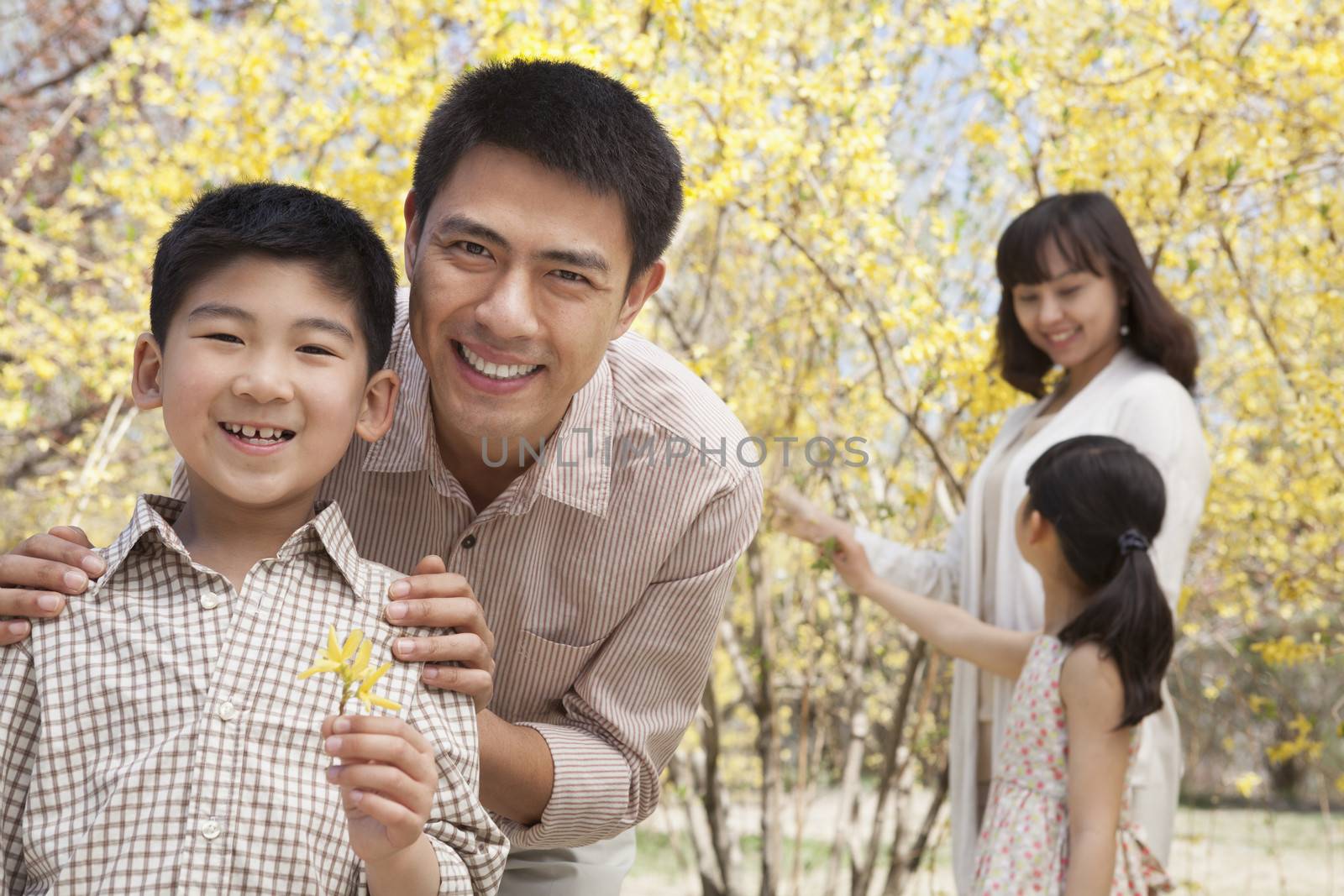 Happy, smiling parents with two children enjoying the park in springtime and looking at flowers by XiXinXing