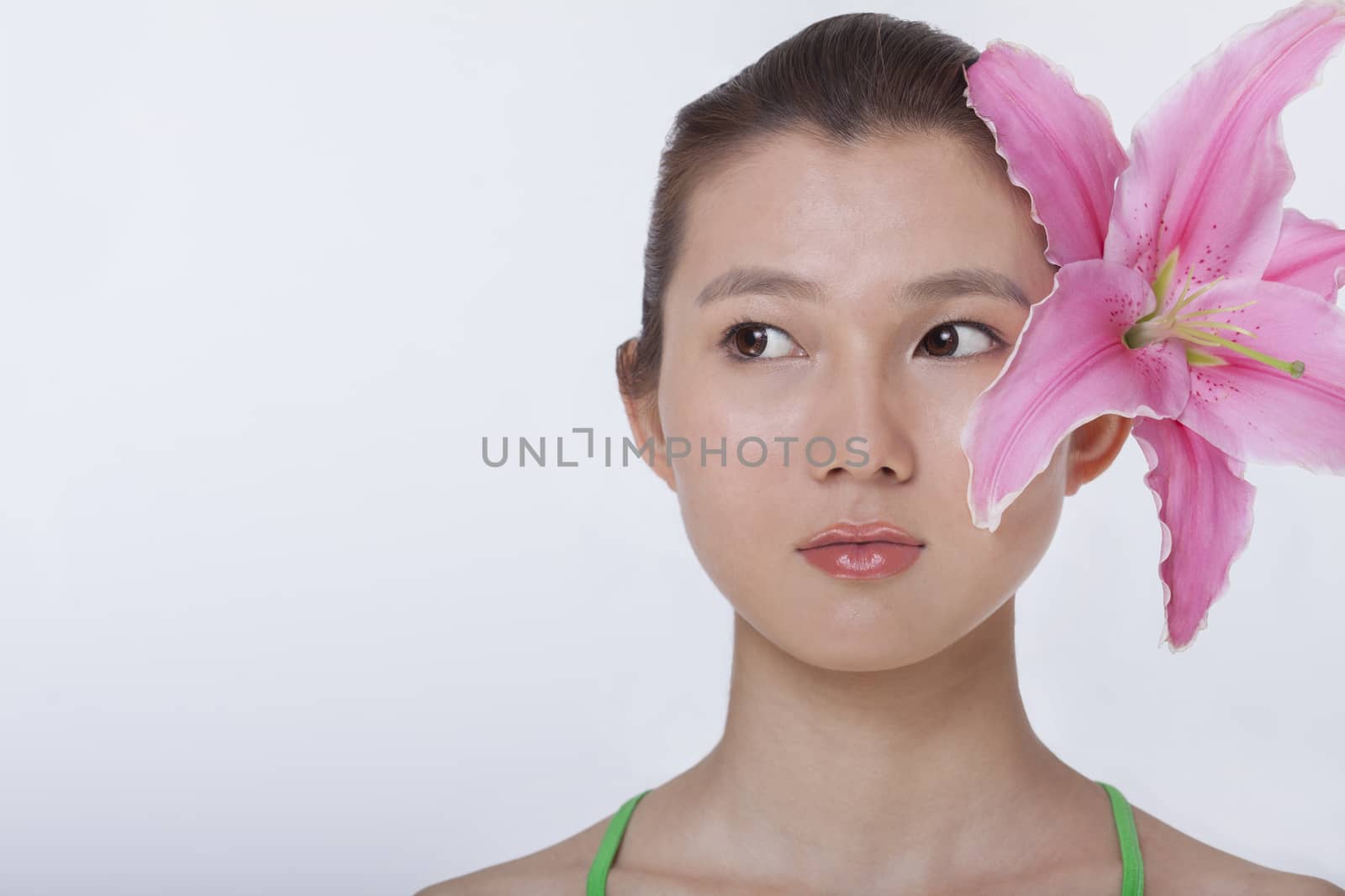 Portrait of young beautiful woman with a large pink flower tucked behind her ear, studio shot by XiXinXing