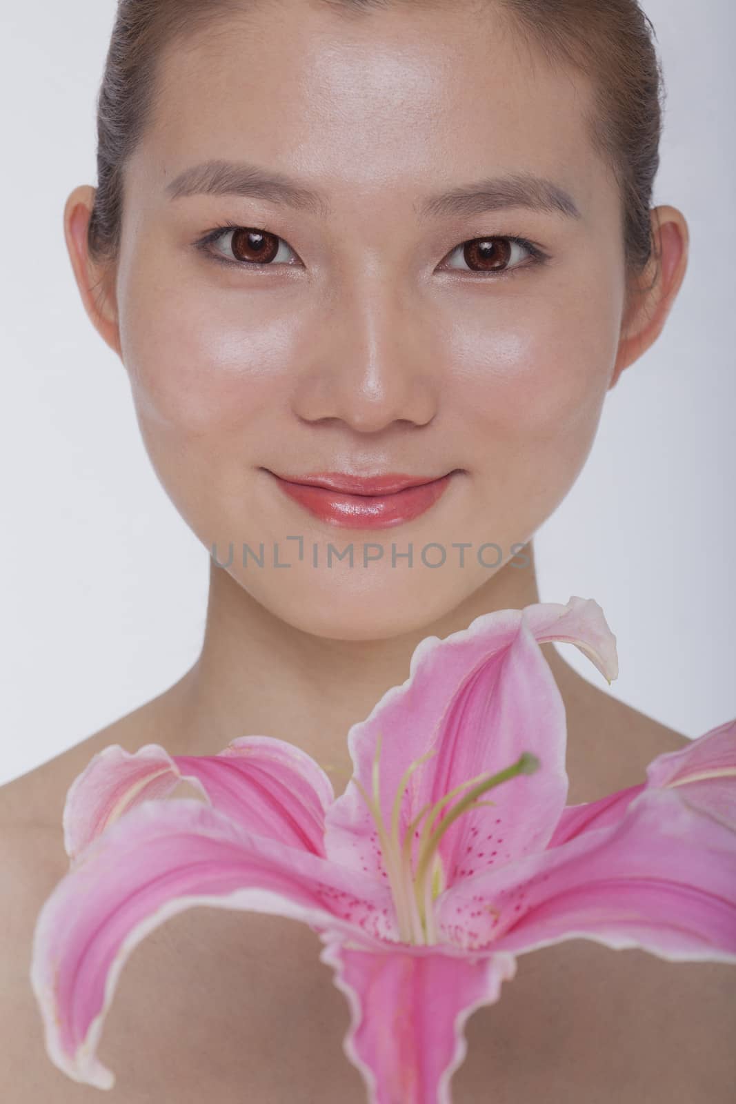 Portrait of young tranquil woman looking at camera with a large pink flower, studio shot by XiXinXing