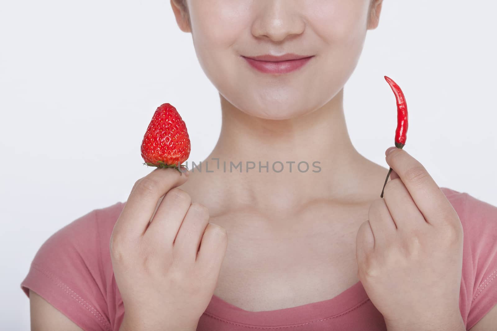 Young woman smiling and holding opposites, a strawberry and a chili pepper, in each hand by XiXinXing