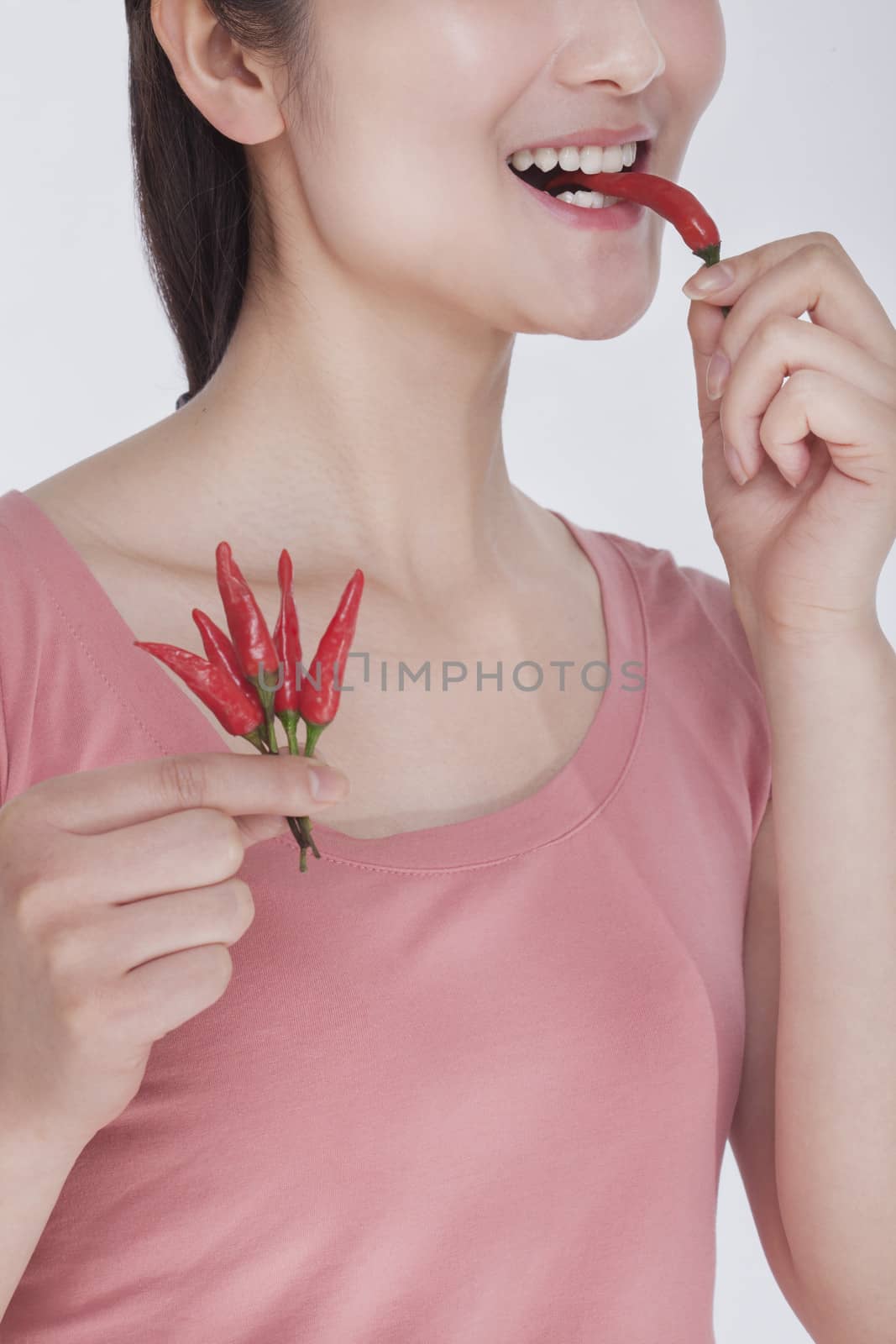 Young woman in pink shirt eating a  chili pepper, studio shot, half face showing by XiXinXing