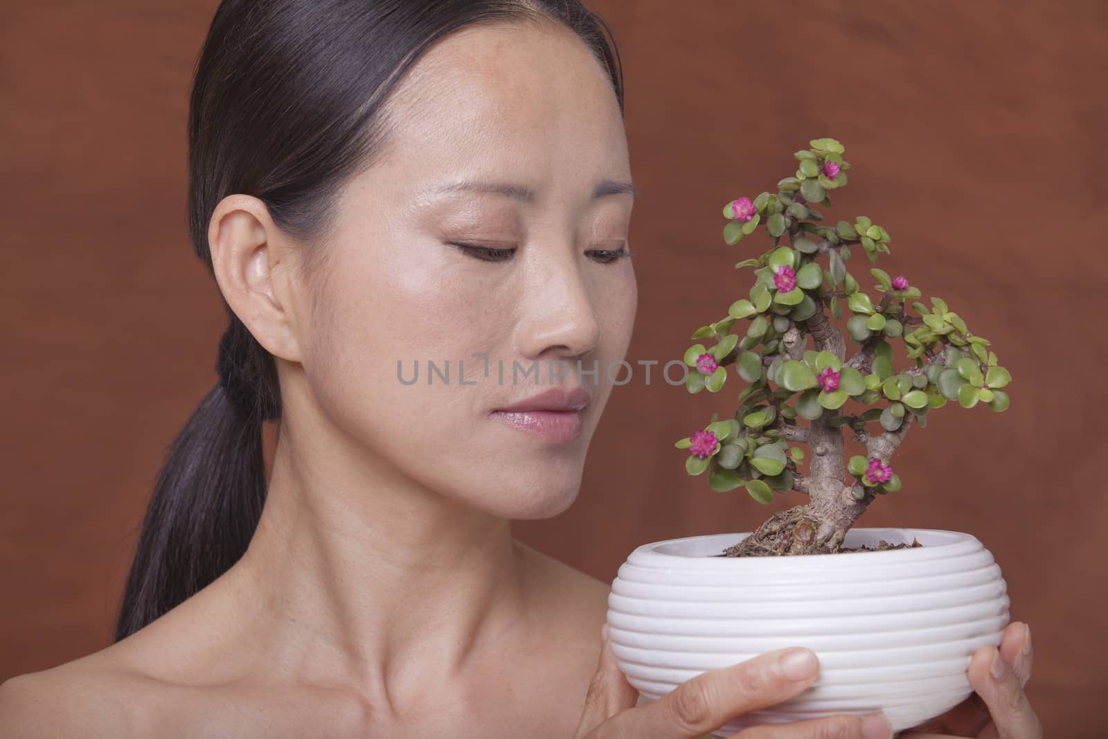 Shirtless woman holding and looking down at a small plant in a flower pot, studio shot by XiXinXing