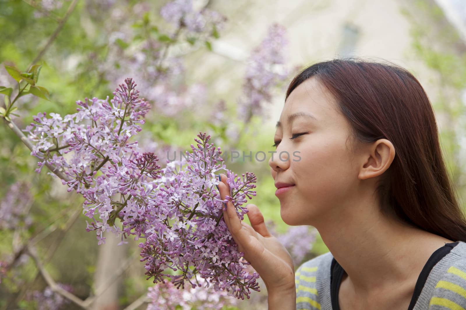 Young woman with eyes closed smelling a flower blossom in the park in springtime