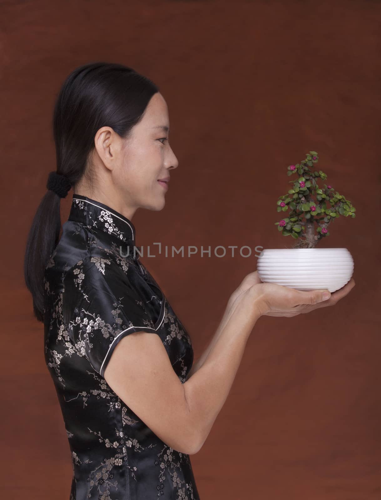 Side view of woman in traditional clothing holding a small plant in a flower pot, studio shot