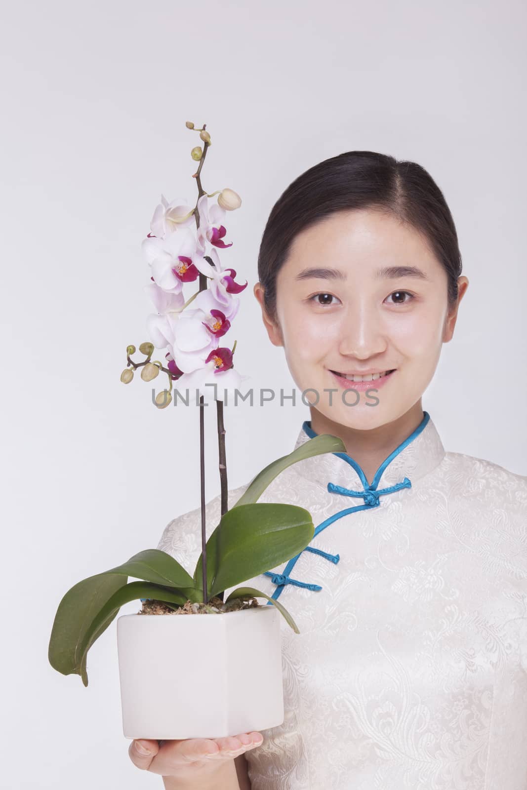 Portrait of smiling young woman holding a beautiful white flower in a flower pot, studio shot by XiXinXing