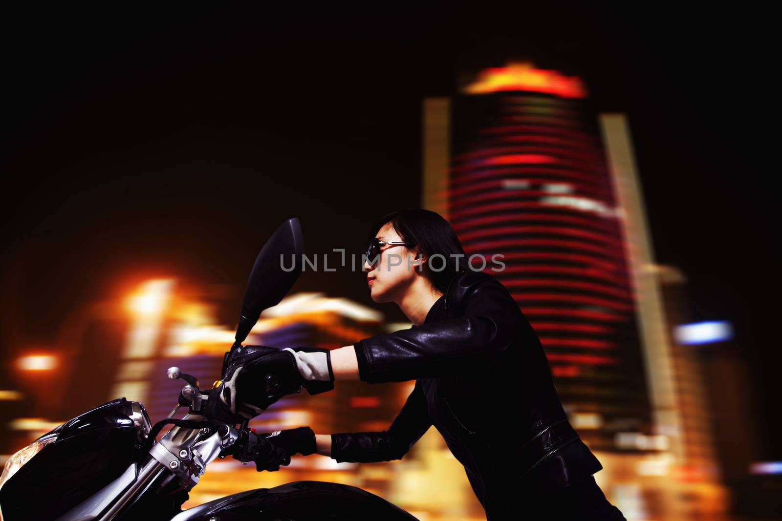 Beautiful young woman riding motorcycle in sunglasses through the city streets at night by XiXinXing