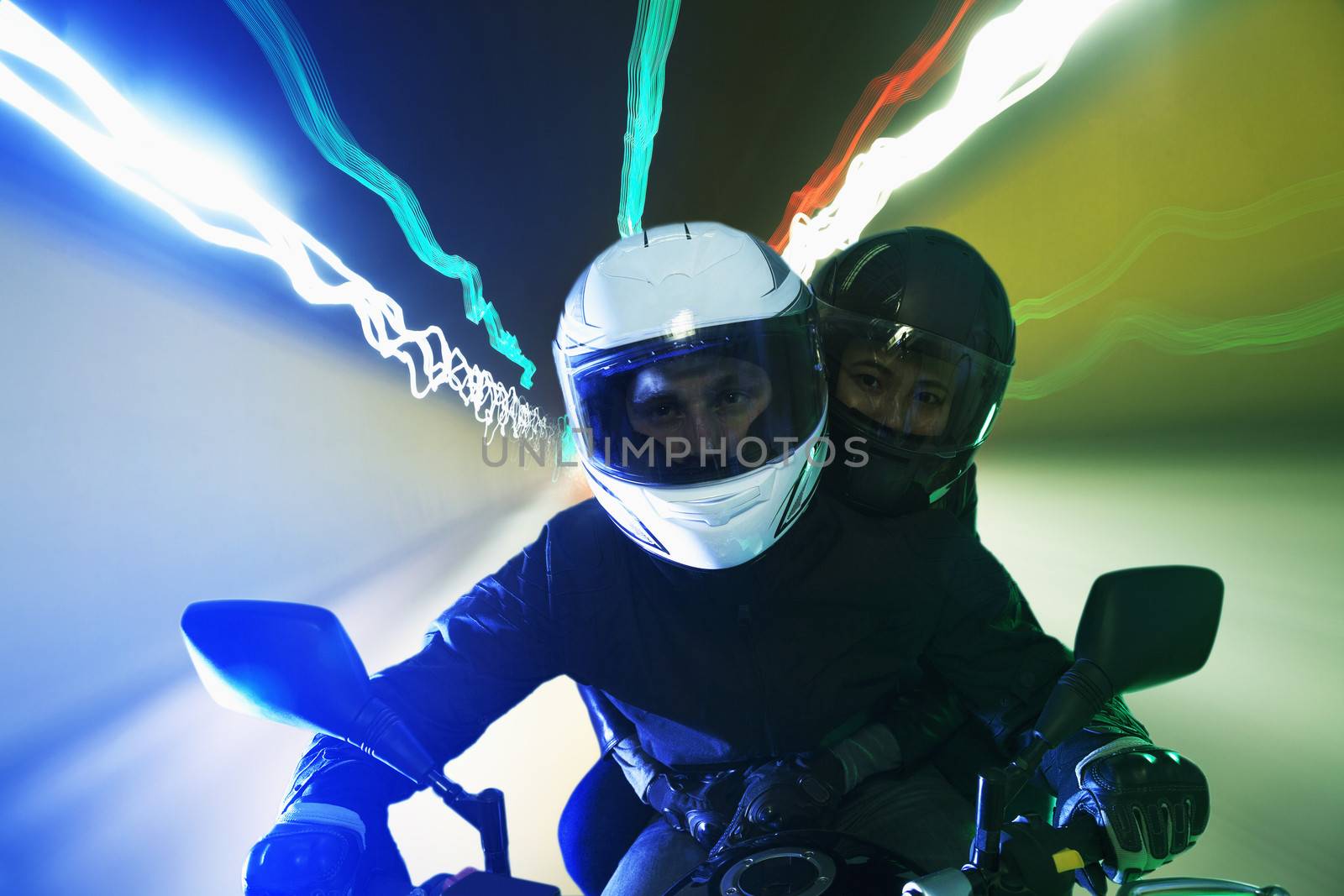 Young couple riding a motorcycle through the city streets at night in Beijing, light trails by XiXinXing