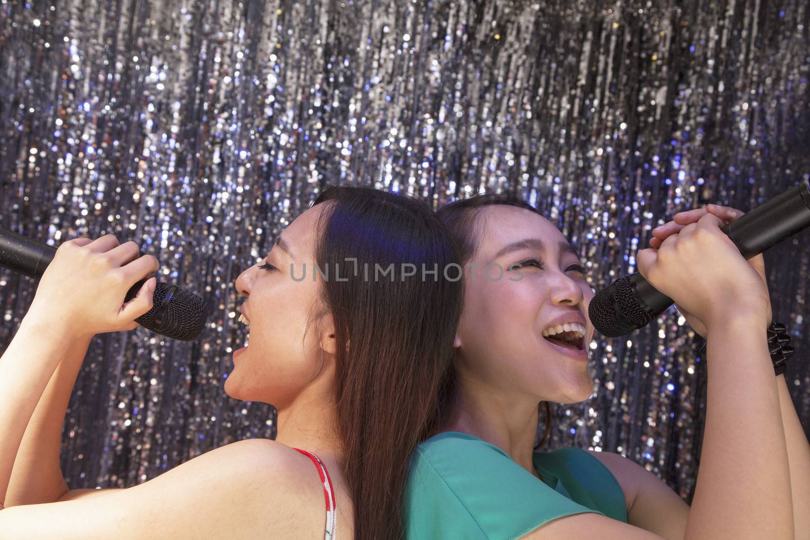 Two friends back to back holding microphones and singing together at karaoke