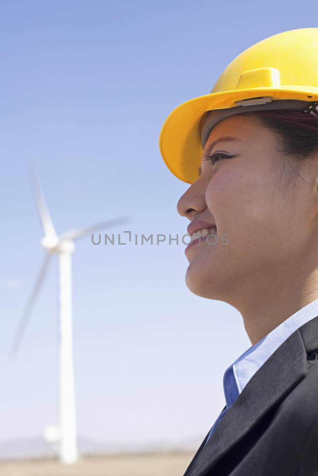 Portrait of young smiling female engineer checking wind turbines on site, side view