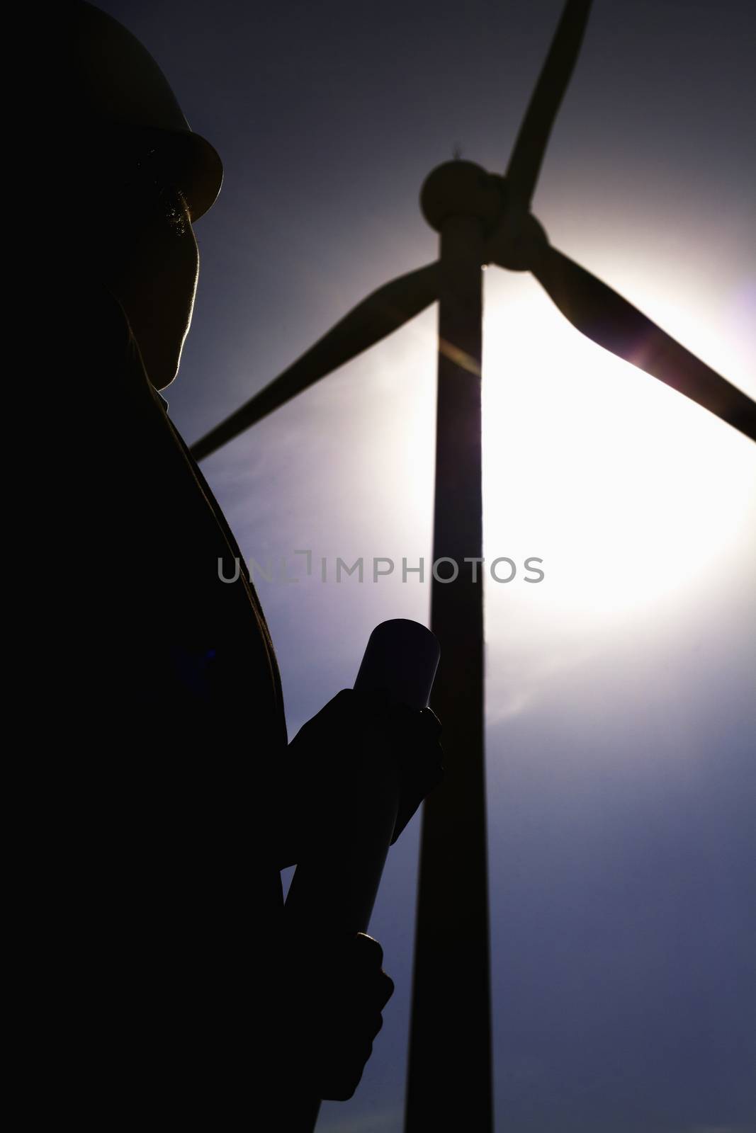 Young female engineer holding blueprints and checking wind turbines on site, silhouette by XiXinXing