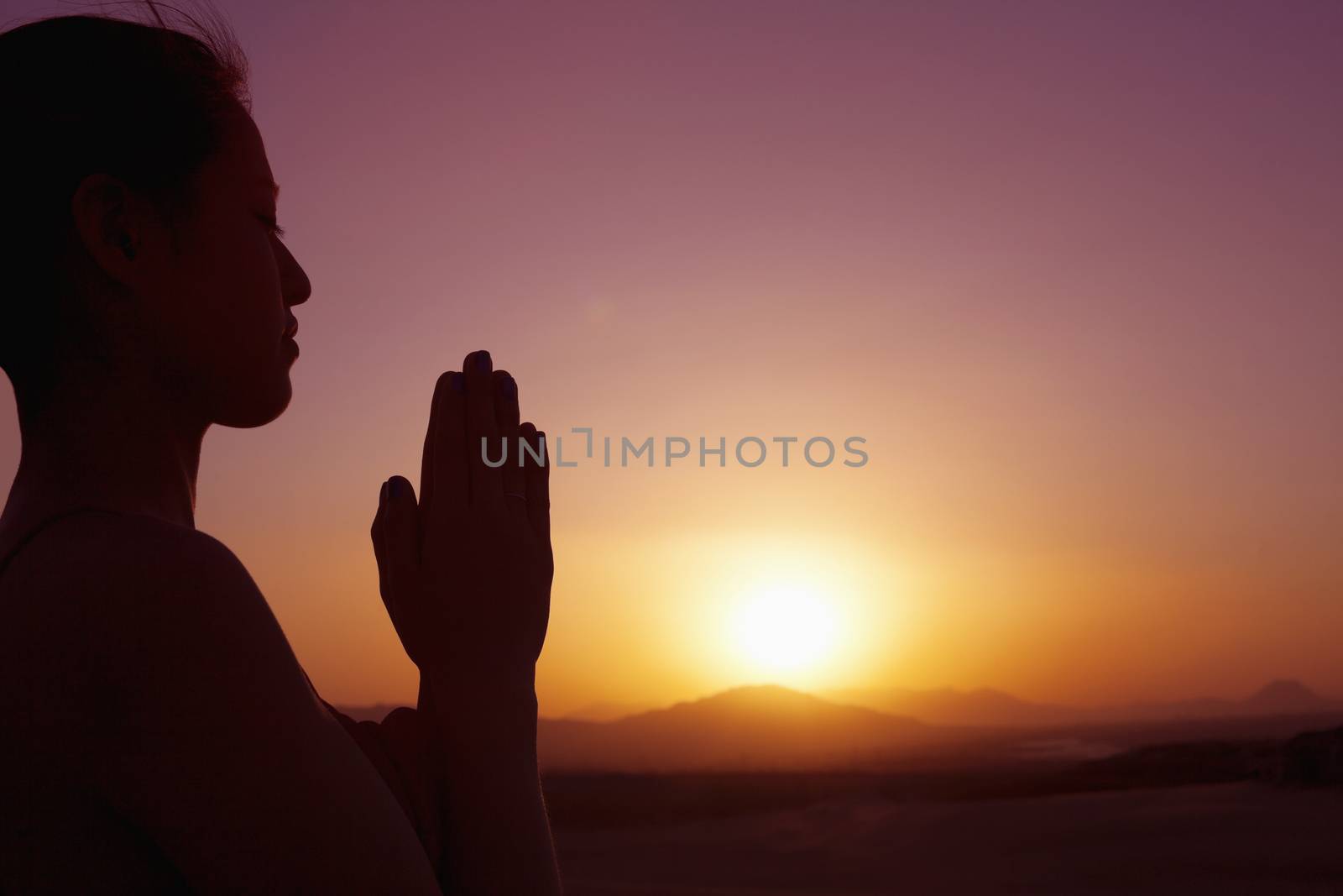 Serene young woman with hands together in prayer pose  in the desert in China, silhouette, sun setting, profile by XiXinXing