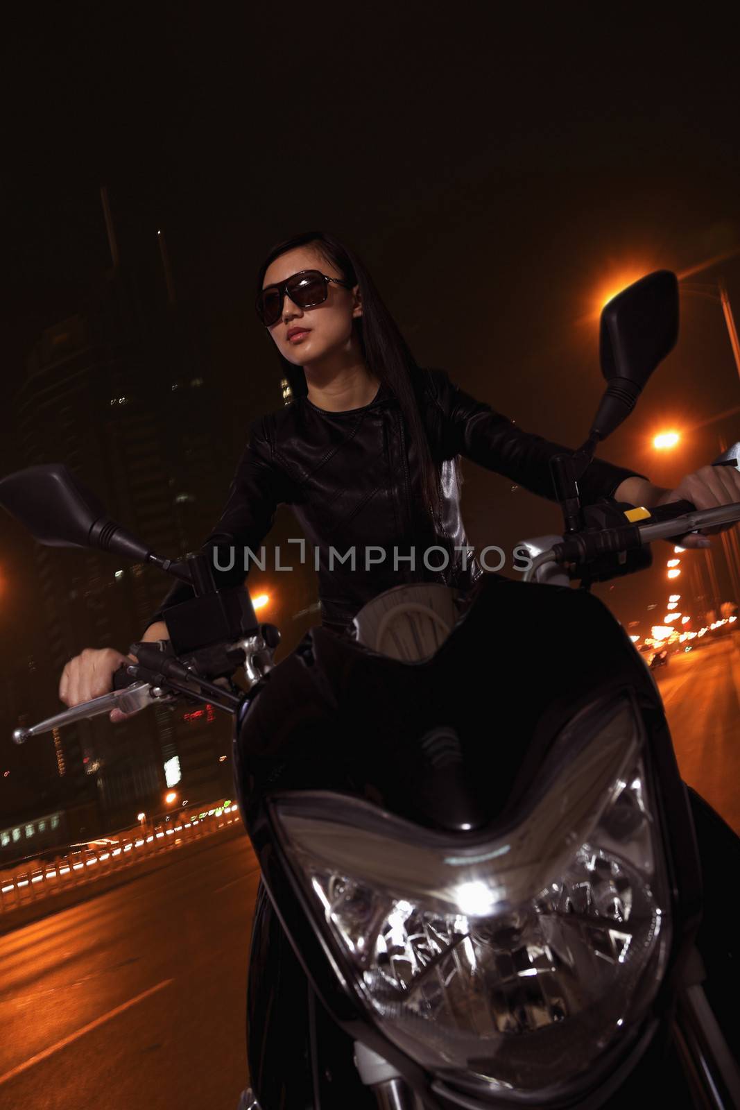 Beautiful young woman riding motorcycle in sunglasses through the city streets at night