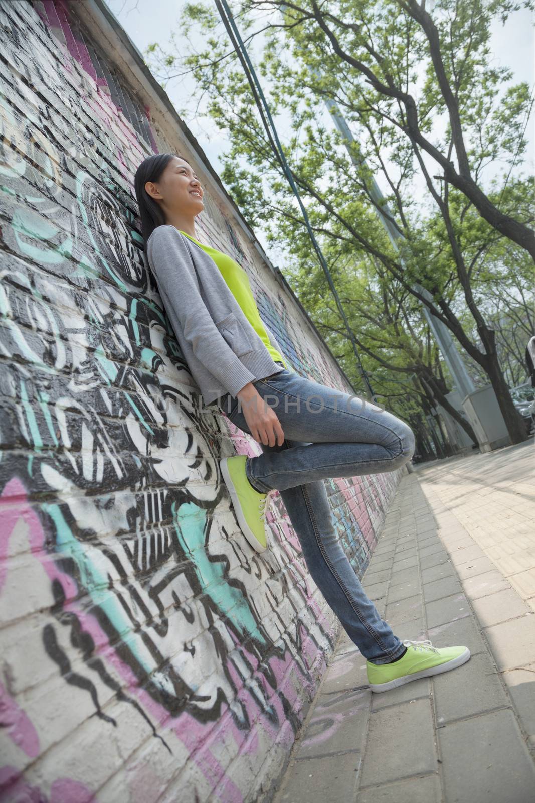 Young woman leaning and hanging out by a wall covered in graffiti