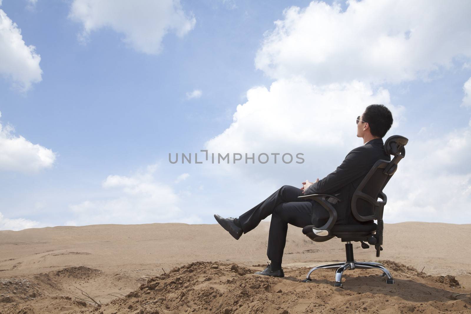 Young businessman sitting in an office chair in the middle of the desert