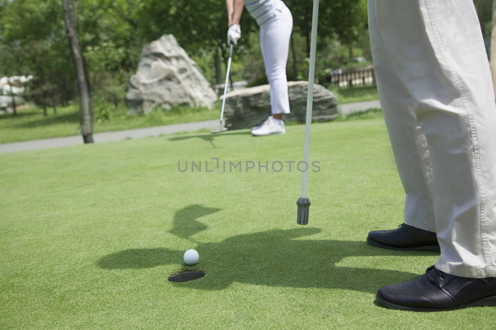 Low section view of man and woman golfing and putting on the golf course