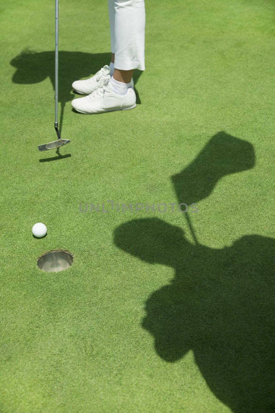 Low section of young woman hitting the ball on the golf course, focus on the hole