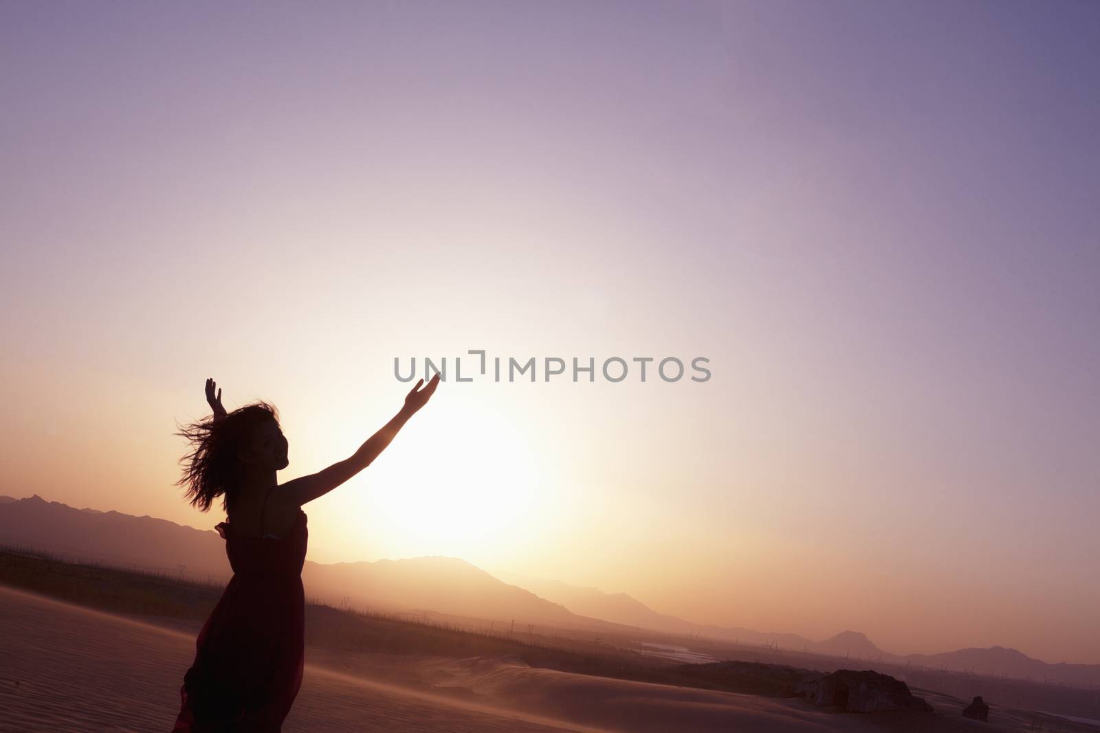 Serene young woman with arms outstretched doing yoga in the desert in China, Silhouette by XiXinXing