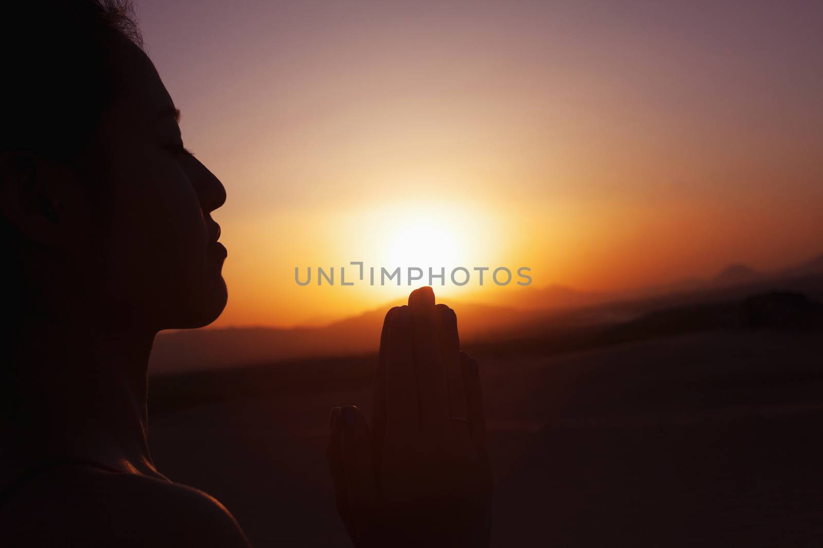 Serene young woman with hands together in prayer pose  in the desert in China, silhouette, sun setting