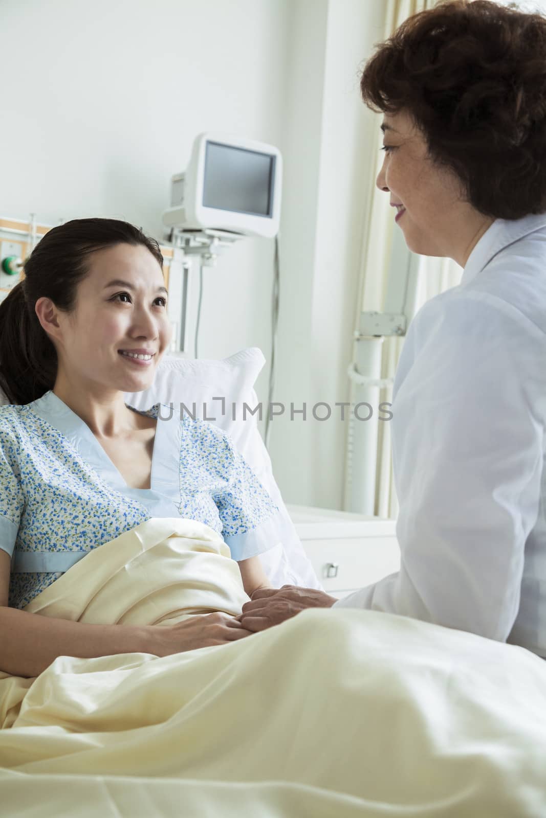 Female doctor sitting on hospital bed and discussing with young female patient by XiXinXing