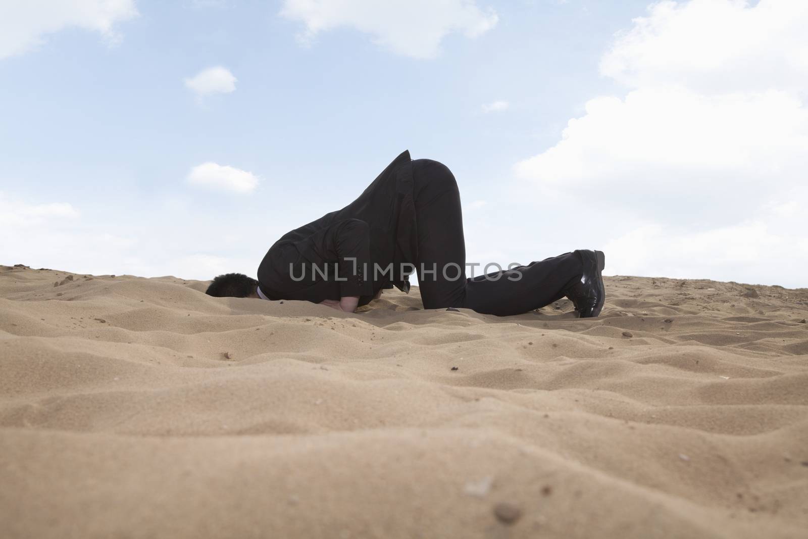 Young businessman kneeling with his head in a hole in the sand by XiXinXing