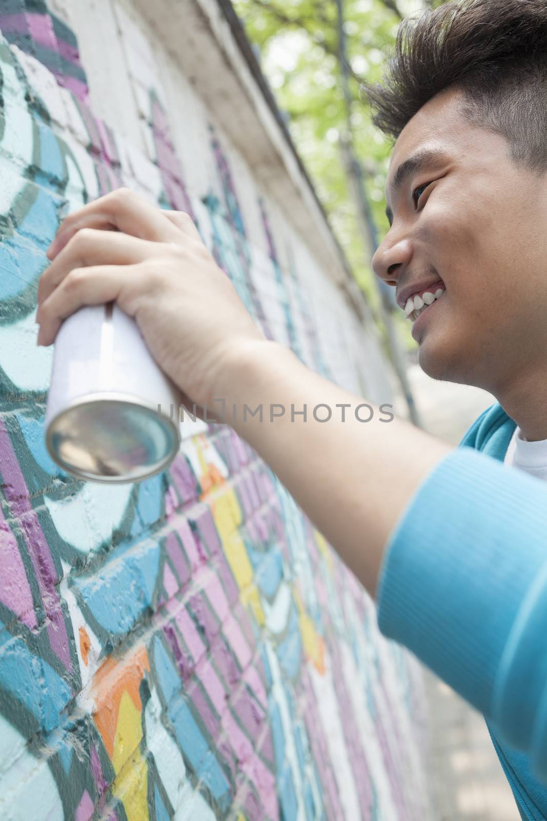 Smiling young man holding a spray can and spray painting on a wall outside