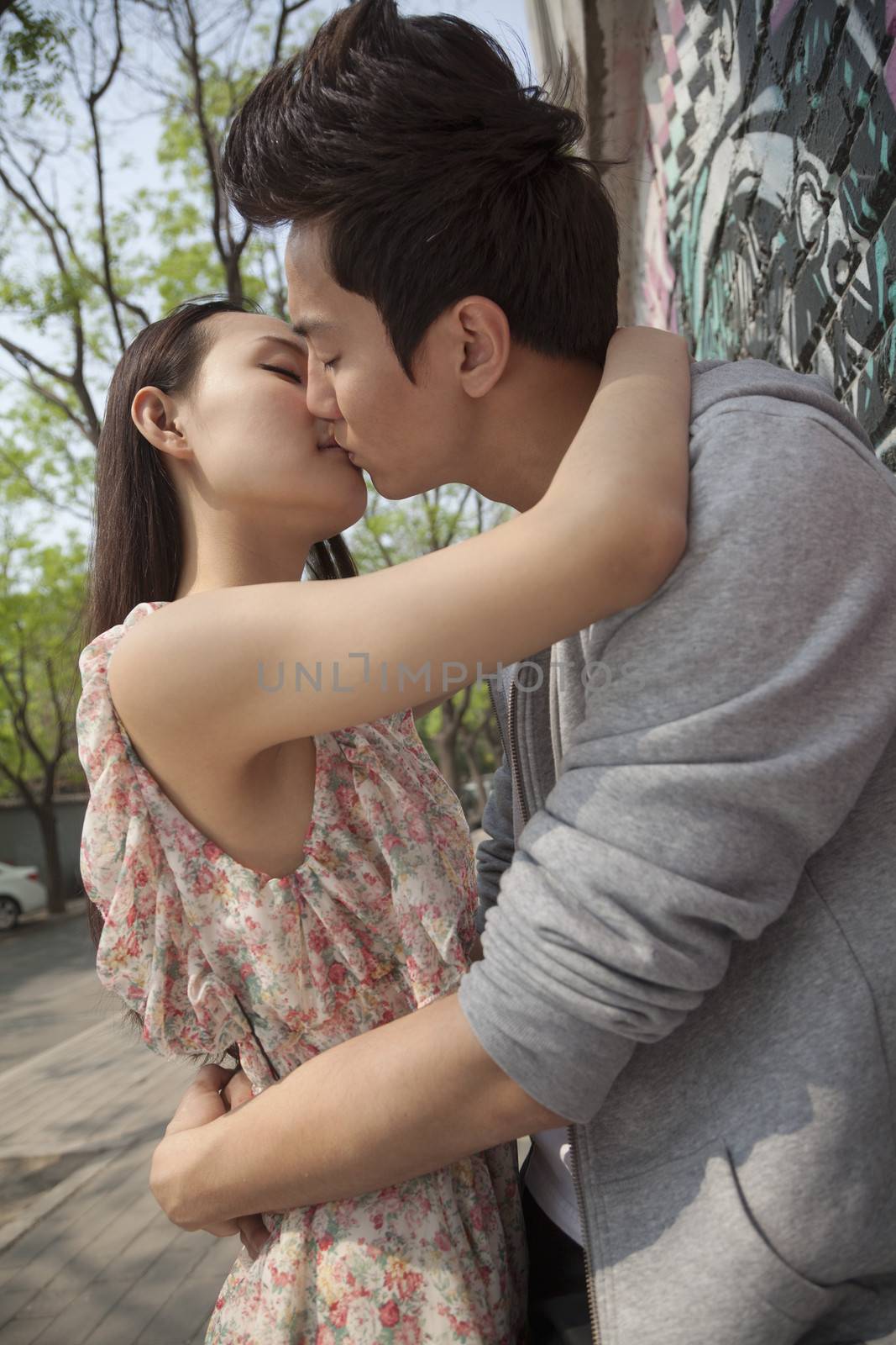 Happy young couple with arms around each other kissing by a wall with graffiti