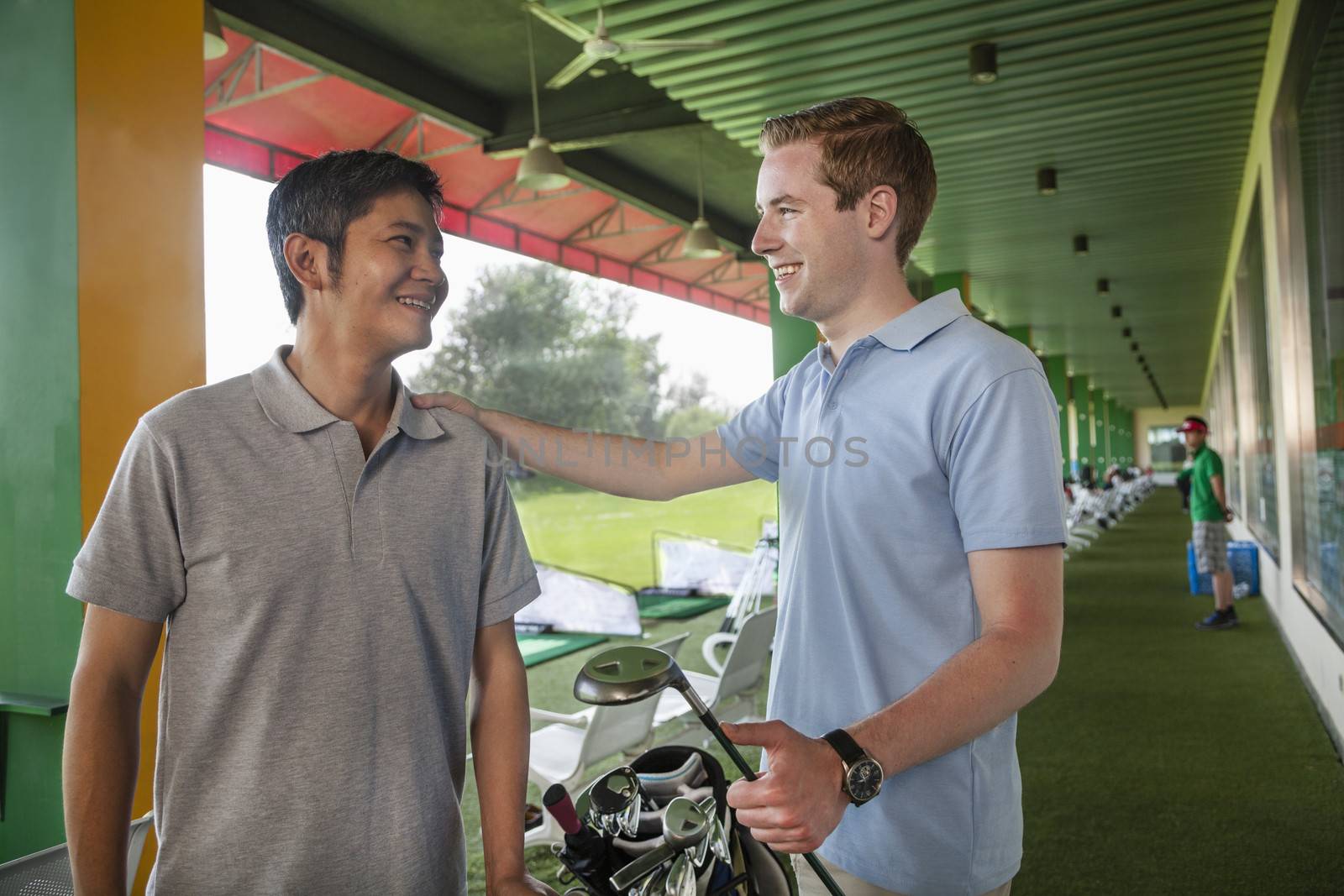 Two male friends talking and smiling while playing golf