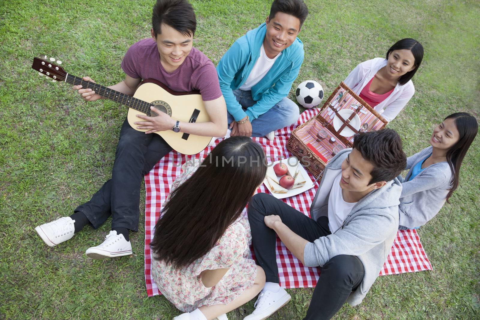 Six friends having a picnic and hanging out in the park, playing guitar and talking by XiXinXing