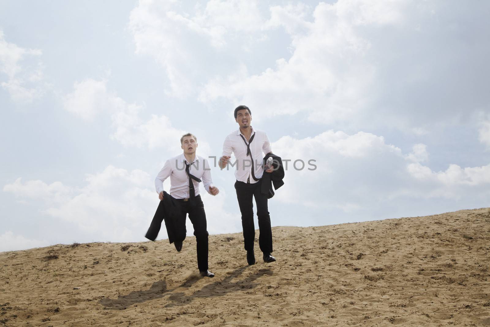 Two young businessmen running and exhausted in the desert, holding jackets by XiXinXing