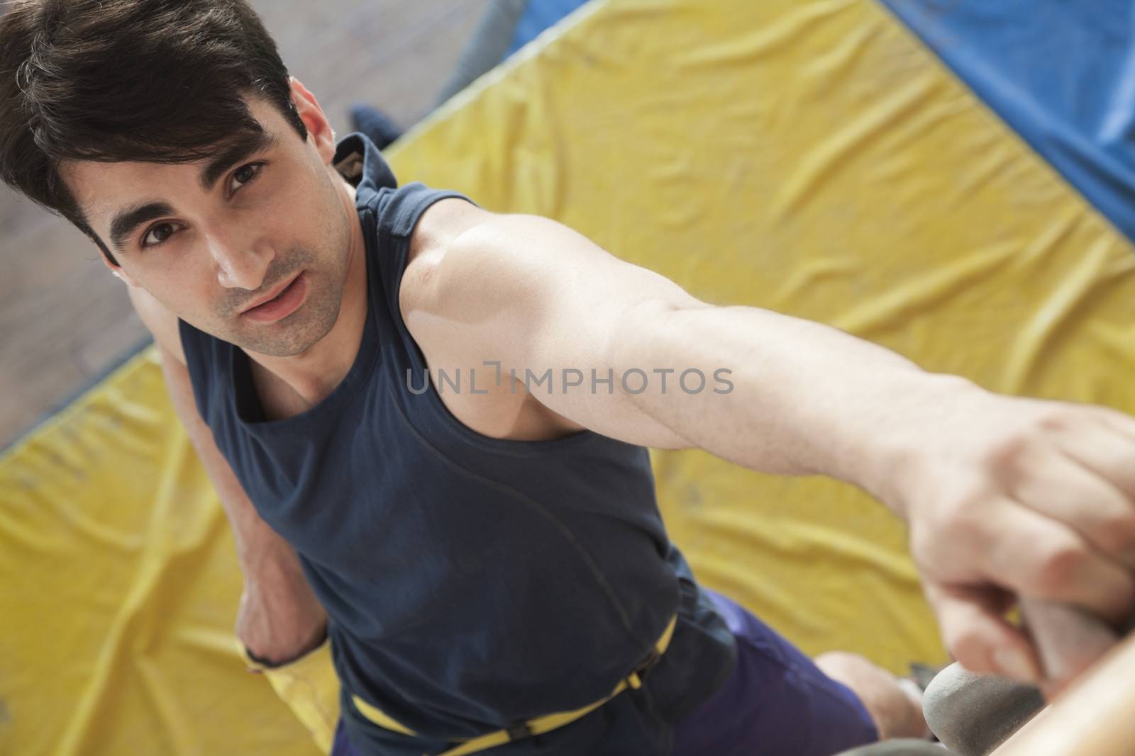 Close-up of young man climbing up a climbing wall in an indoor climbing gym, directly above