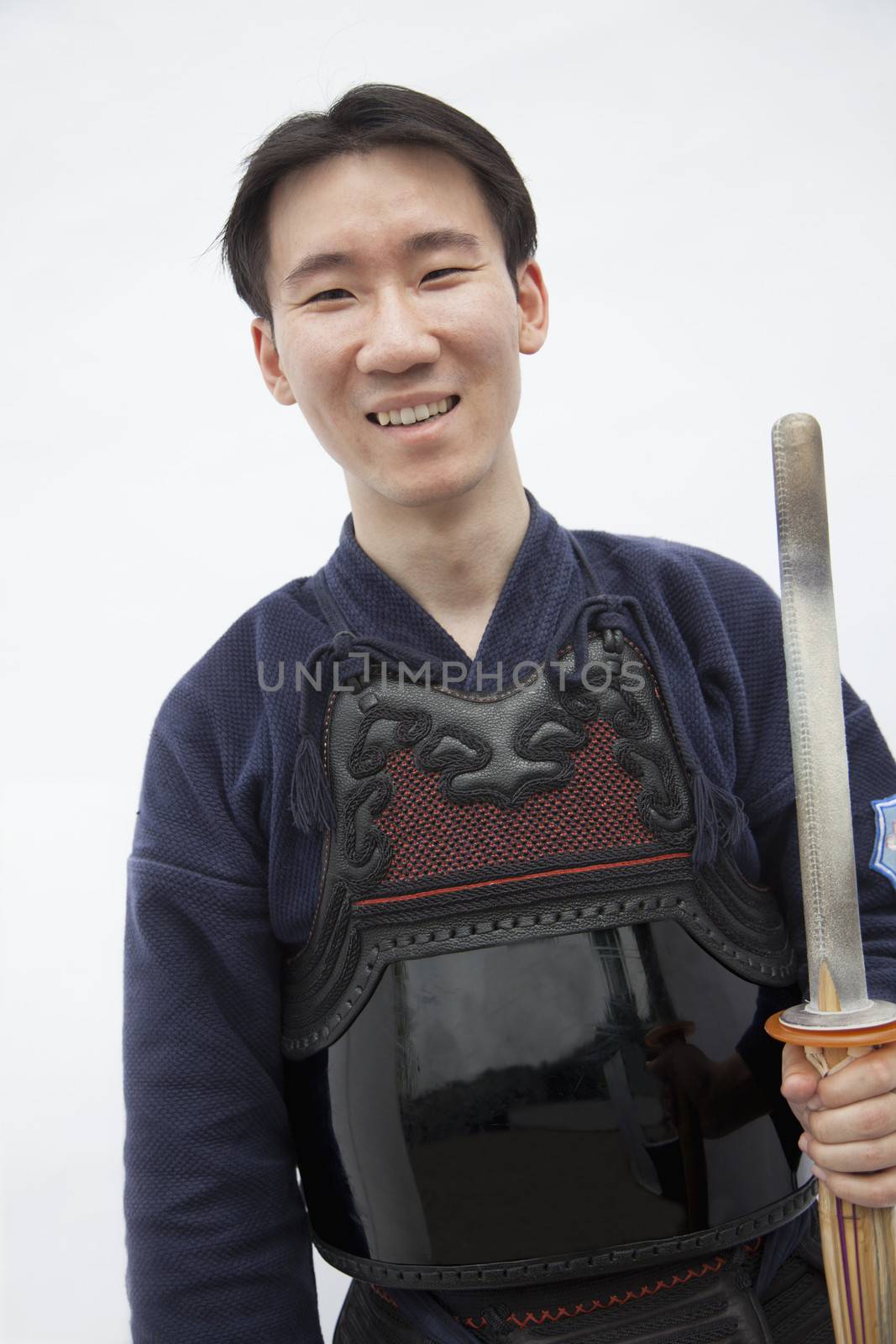 Portrait of young smiling man in traditional Japanese clothing holding a sword, studio shot