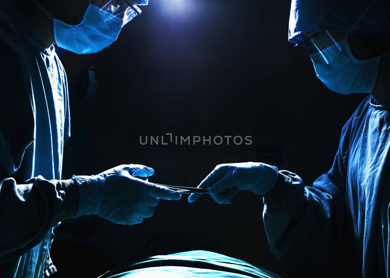 Two surgeons working and passing surgical equipment in the operating room, dark 