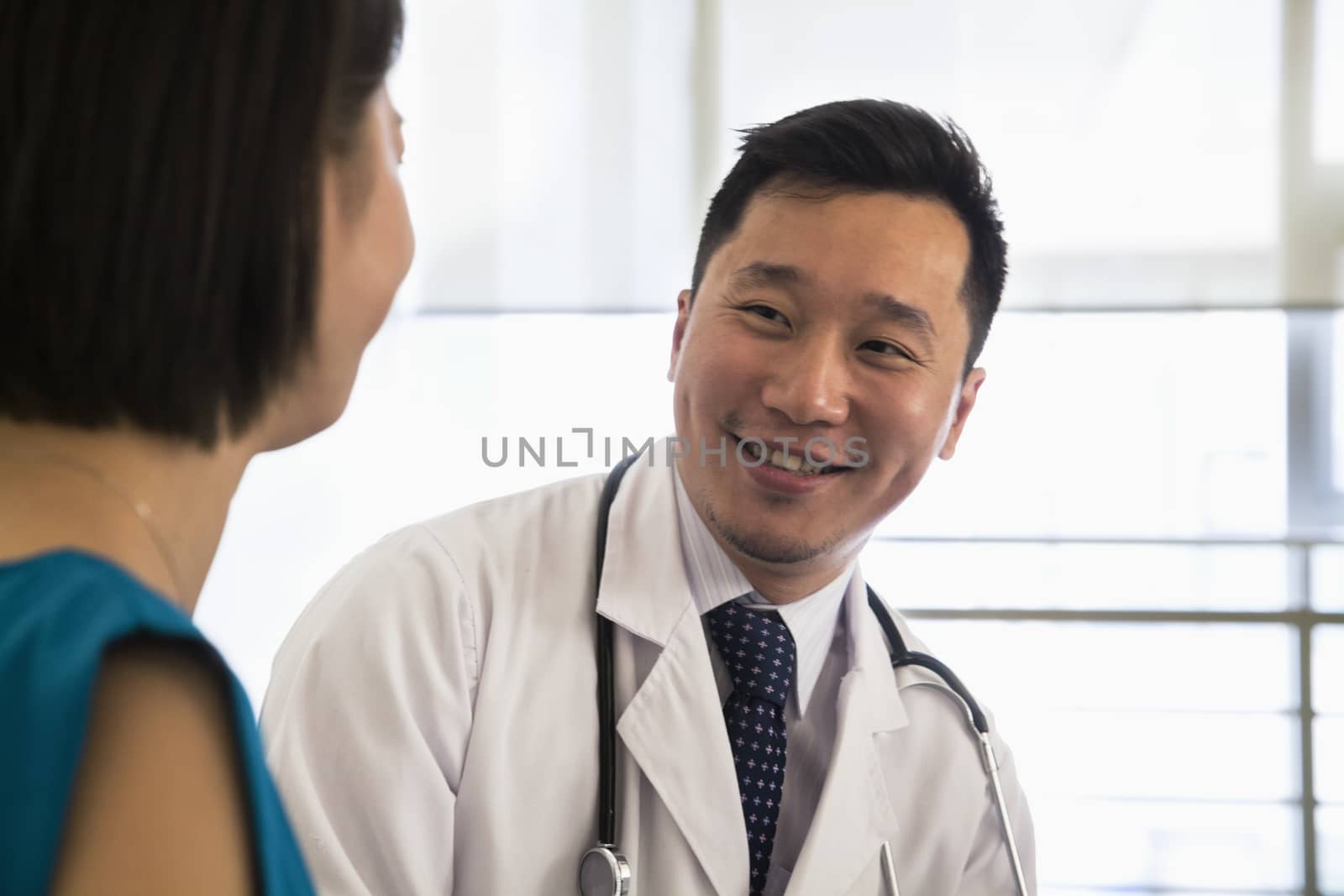 Smiling doctor sitting down and consulting patient in the hospital, close-up