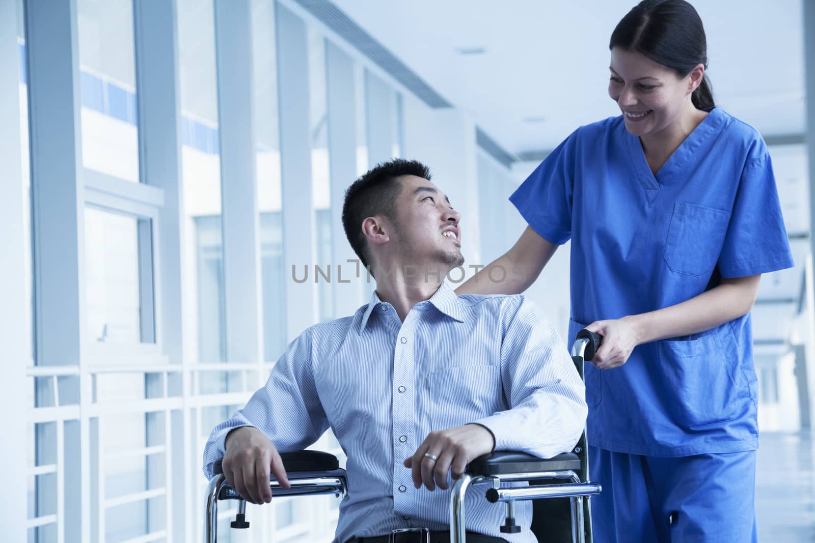 Smiling female nurse pushing and assisting patient in a wheelchair in the hospital 