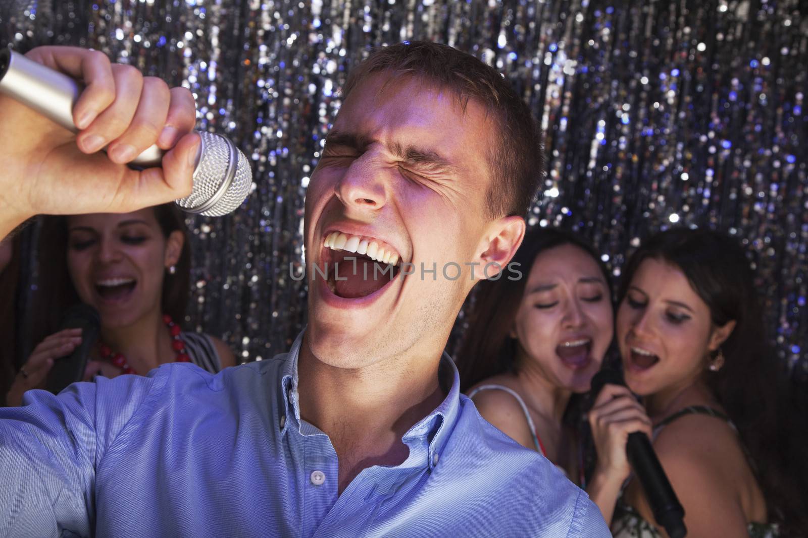 Young man singing into a microphone at karaoke, friends singing in the background