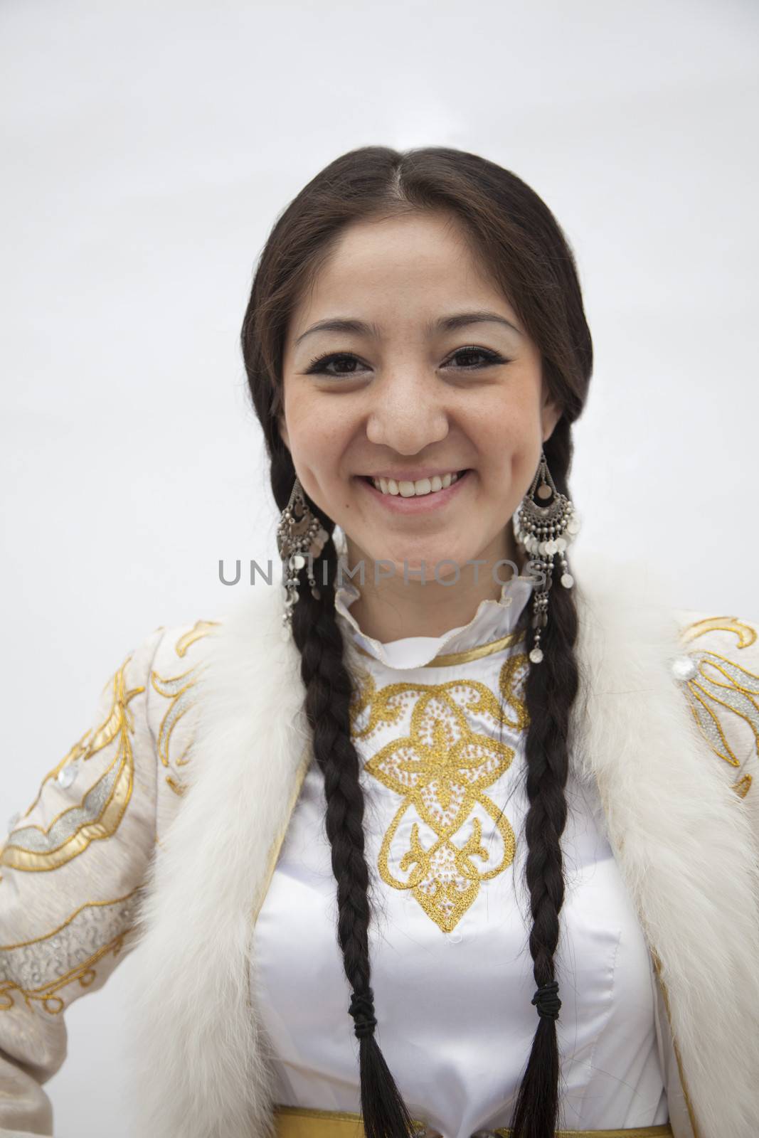 Portrait of young smiling woman with braids in traditional clothing from Kazakhstan, studio shot