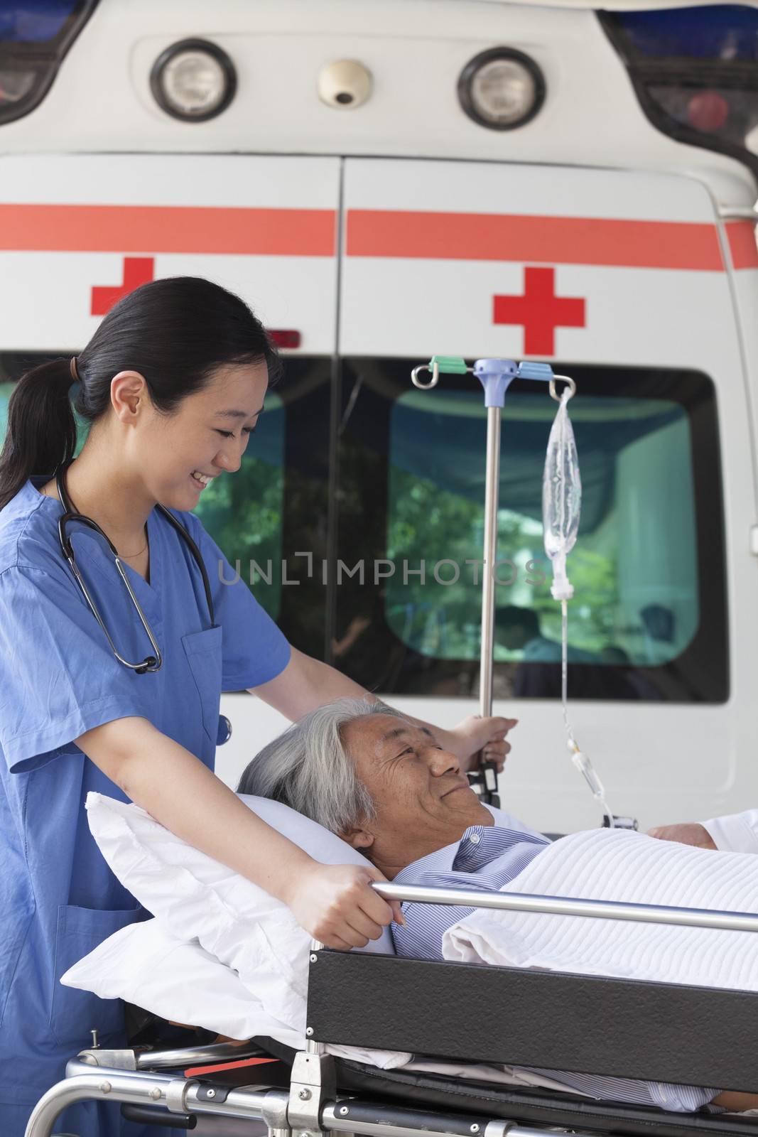 Female paramedic wheeling in a elderly patient on a stretcher in front of an ambulance