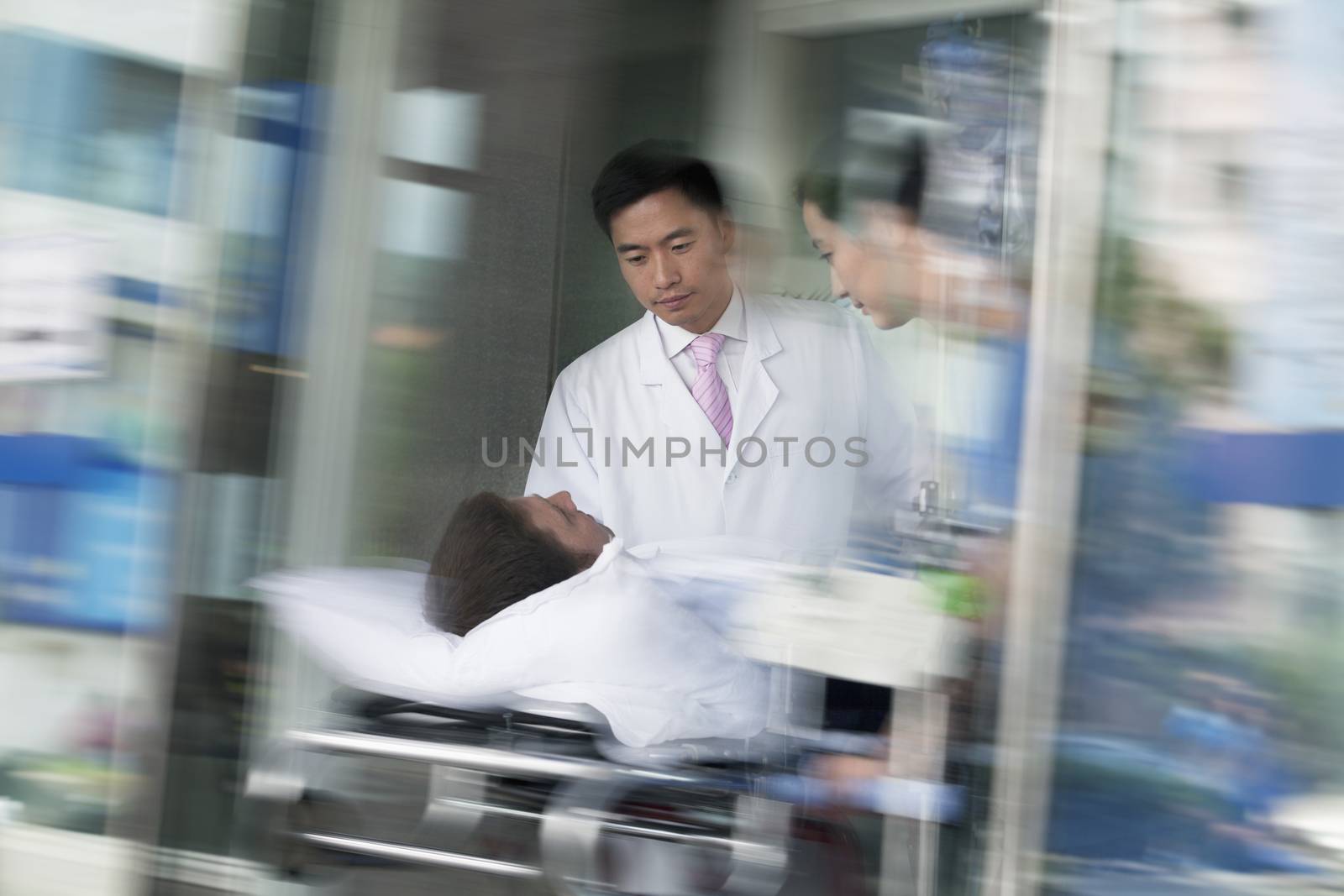 Two doctors wheeling in a patient on a stretcher through the doors of the hospital by XiXinXing